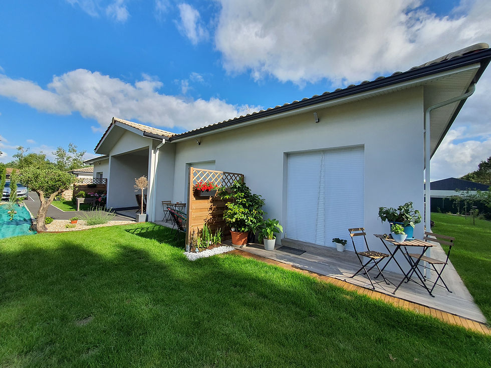Maison blanche moderne avec terrasse, plantes en pots et table de jardin, sous un ciel bleu nuageux.