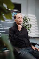 Alexander Khramtsov, Geschäftsführer der SFP-IT GmbH, sitzt in einer Interview-Situation und blickt seitlich in die Kamera, professionell ausgeleuchtet.