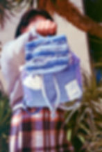 Stylish model gIrl holding backpack made of distressed upcycled denim towards the fashion photographer.