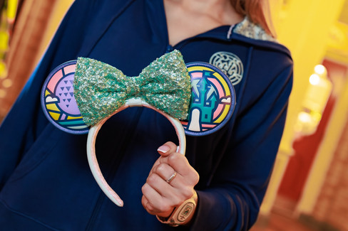 Close up of Minnie Mouse ears with stained glass park icons and a green sequin bow.
