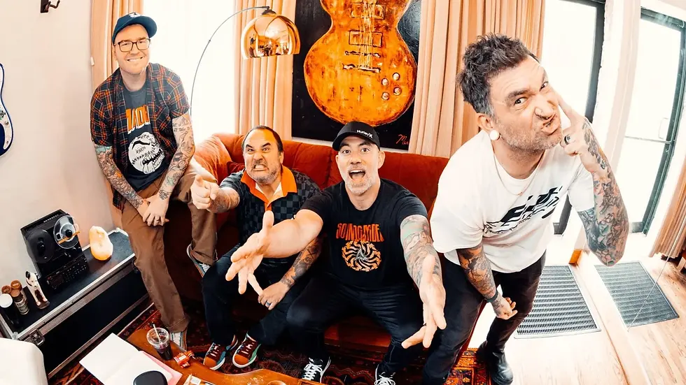 Four tattooed men pose playfully in a room with a red sofa, orange guitar art, and striped rug. Two wear black shirts, one a plaid shirt, and one a white tee. New Found Glory was just added to the Eat to the Beat concert series at EPCOT. 
