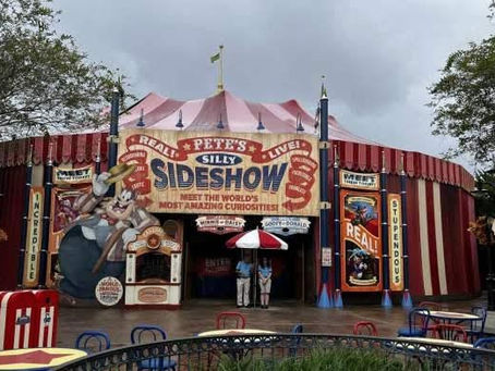 The exterior of the Pete’s Silly Sideshow tent in Storybook Circus at Magic Kingdom, featuring a large banner with a character of Pete as the ringmaster and a list of acts including the "Dashing Disney Pals" and "Daring Disney Pals".