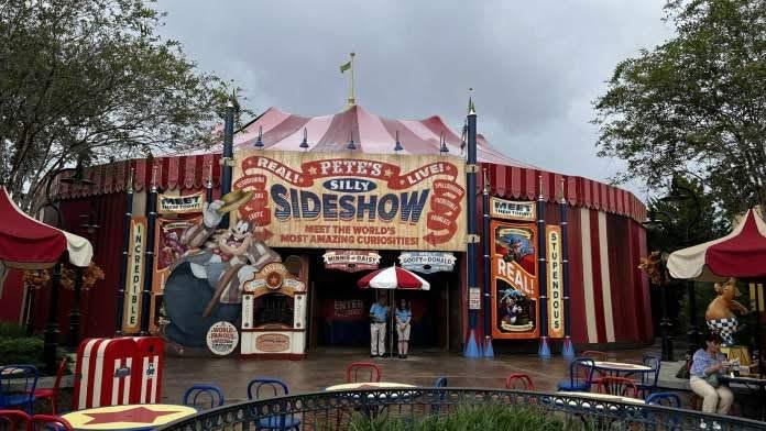 The exterior of the Pete’s Silly Sideshow tent in Storybook Circus at Magic Kingdom, featuring a large banner with a character of Pete as the ringmaster and a list of acts including the "Dashing Disney Pals" and "Daring Disney Pals".