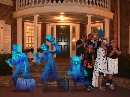 At Mickey’s Not-So-Scary Halloween Party, a group of costumed guests stand outside a brick building at night, posing alongside the ghostly Hitchhiking Ghosts from the Haunted Mansion, added as glowing blue holographic effects.