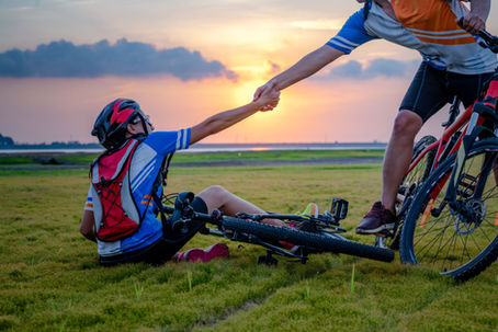 A bike rider has fallen and another bike rider is reaching out a hand to pull him up.