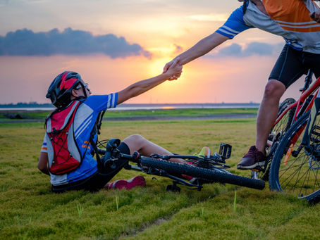 A bike rider has fallen and another bike rider is reaching out a hand to pull him up.