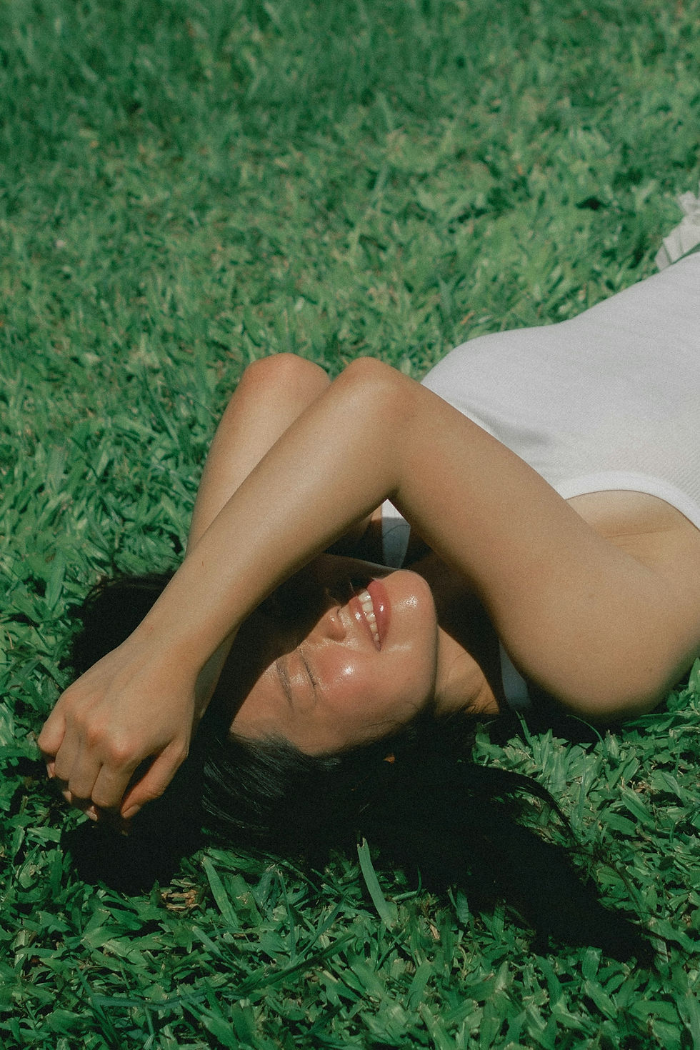 A girl lying on the grass, covering her face with her arms