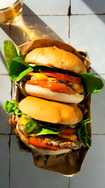 Professionelle Food-Fotografie von zwei Cheeseburgern auf einem schlichten Hintergrund, ideal für Restaurantmenüs und kulinarische Präsentationen.