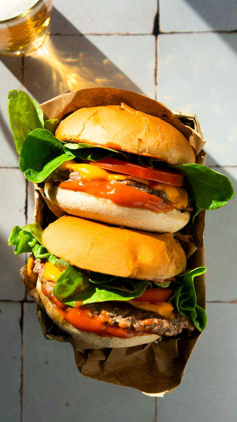 Professionelle Food-Fotografie von zwei Cheeseburgern auf einem schlichten Hintergrund, ideal für Restaurantmenüs und kulinarische Präsentationen.