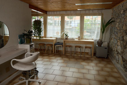 Friseurstuhl mit Spiegel und angrenzenden Café-Tischen vor dem Fenster im Haarcafé