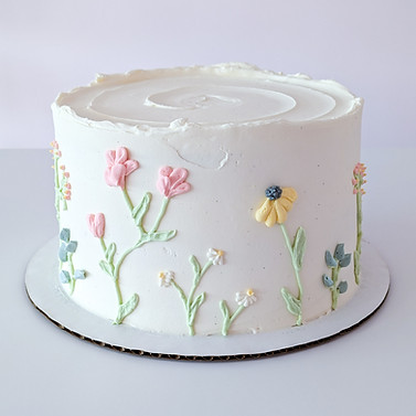 Photo of a cake with pastel colored wildflowers piped around the sides in buttercream