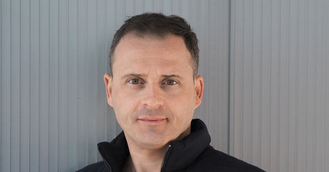 Portrait of Ondrej Chudy, Managing Director at TMD, standing in front of a grey vertical-panel facade. Wearing a black vest and T-shirt, reflecting his role in Architecture & CGI