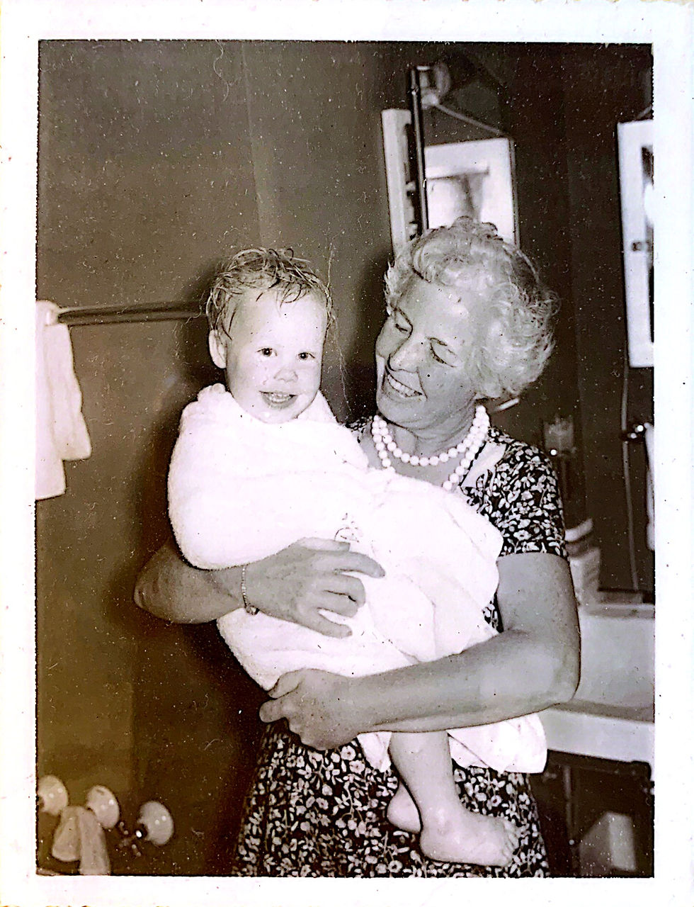 Grandmother in chunky pearls holding baby girl wrapped in towel.
