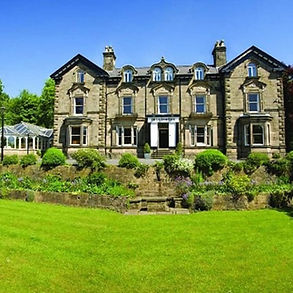 a country house built of grey limestone seen across a wide grass lawn