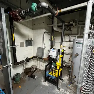 Black gas lines with yellow "NATURAL GAS" labels and valves installed on a stainless steel wall in a commercial kitchen next to a cooking range.
