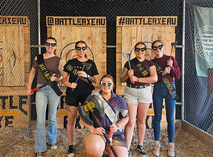 A group of 5 women after a hen's party session, holding axes and wearing matching bridesmaid sunglasses, with the bride to be in the middle.