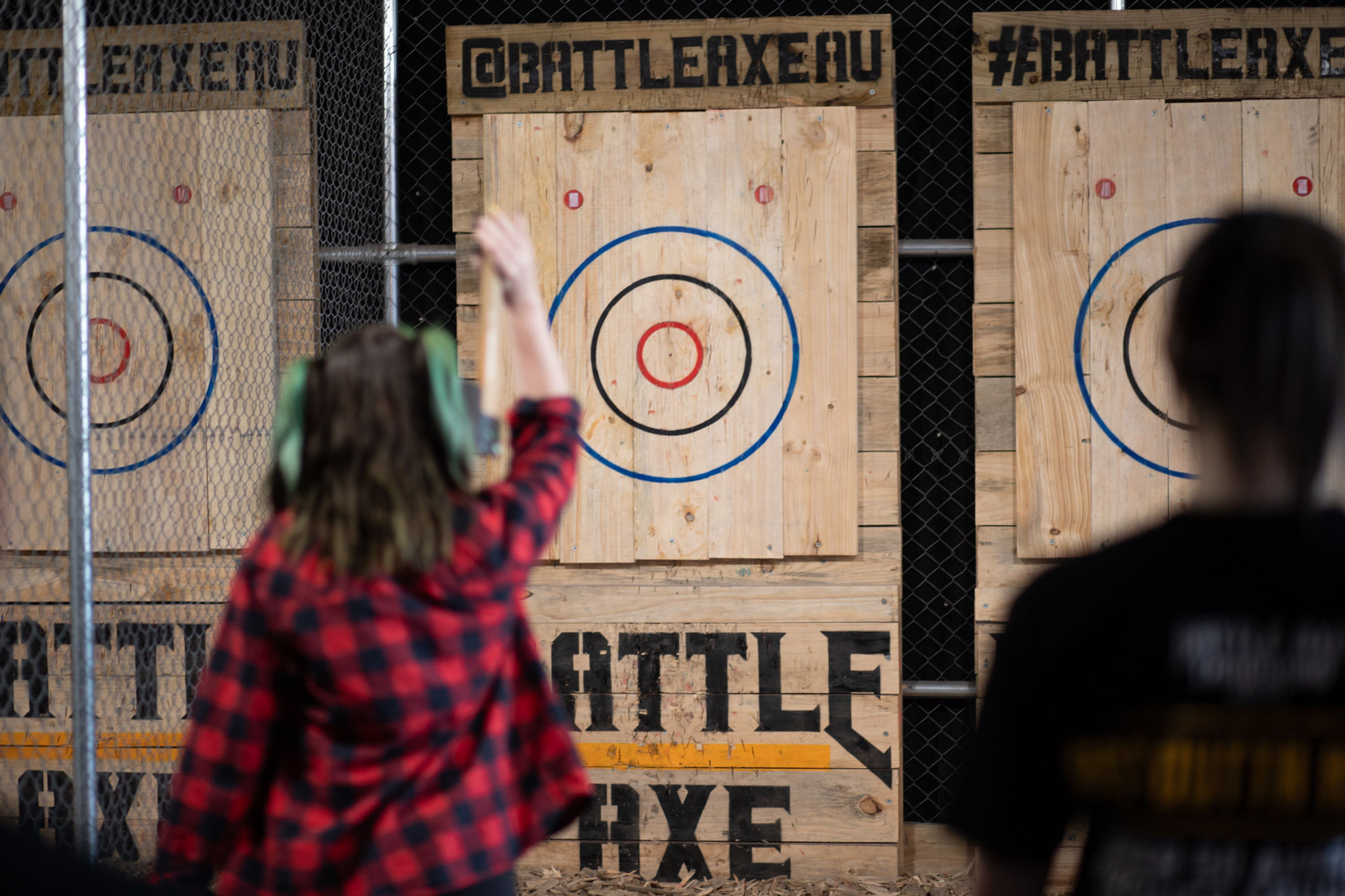 Person in a red and black plaid shirt throwing axes during league at Battle Axe Throwing