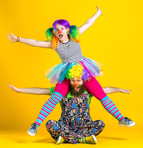 two adults in clown costumes, one sat down and one jumping