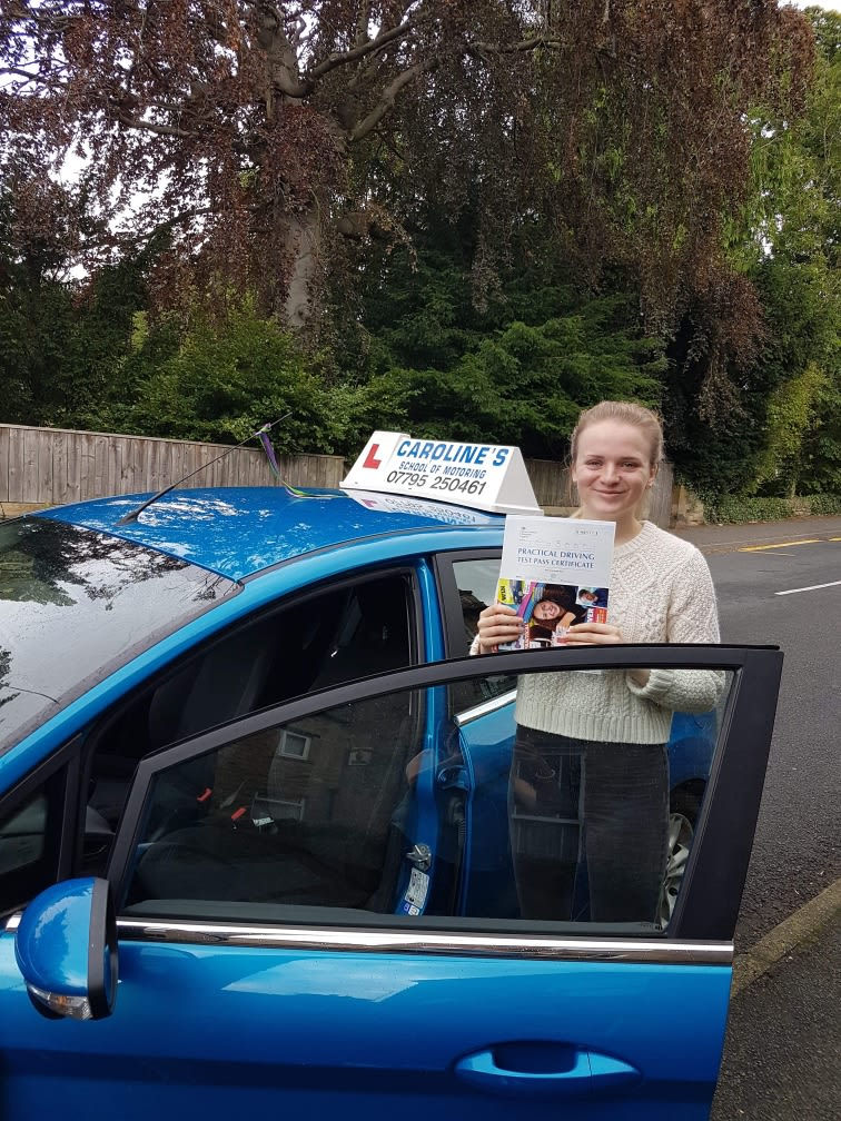 Female driver stood next to blue car, holding driver training booklet