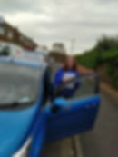 Woman stood behind blue car door, holding pass certificate
