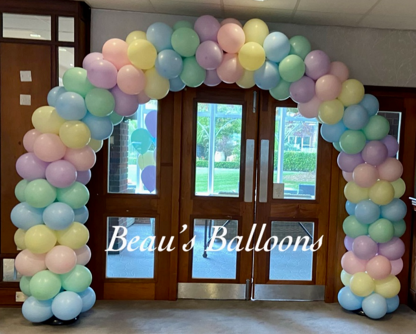 Pastel coloured balloon arch in front of brown wooden doors