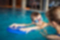 Boy with swimming goggles on in pool, looking at teacher