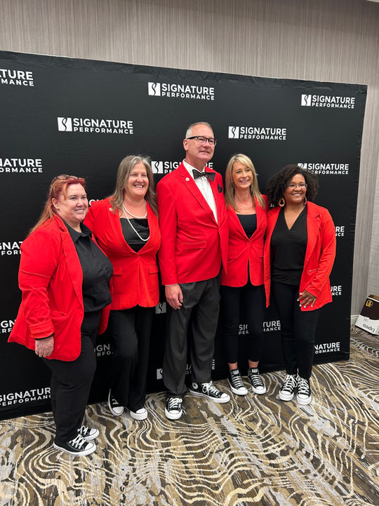 Signature Performance team posing in red attire at a company event