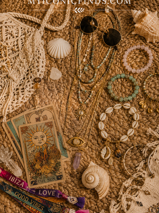 Bohemian-inspired flat lay featuring tarot cards, layered jewelry, seashells, crystal pendants, sunglasses, woven accessories, and festival wristbands arranged on a natural woven surface.