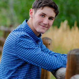 boy leaning against fence in blue plaid shirt