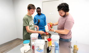 Participant souriant à une table avec du matériel de cuisine lors d’une activité culinaire à S.Au.S.