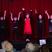 Children performing choreography together on stage during a musical theatre production.