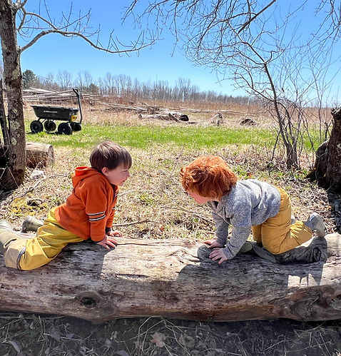 Boy with therapeutic needs sitting on a log, engaging with a peer during an inclusive enrichment program