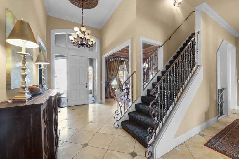 Elegant home foyer with staircase, chandelier, and a welcoming open door