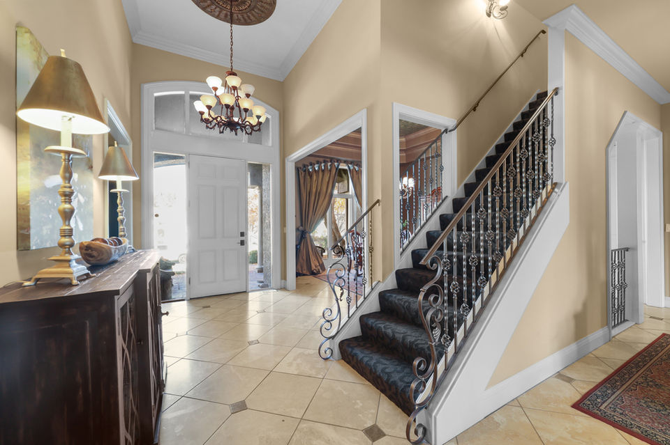 Elegant home foyer with staircase, open door, and decorative chandelier.