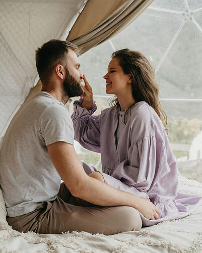 Couple facing each other in a tent with woman in purple dress touching man’s nose