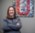 A clinical athletic trainer smiling in front of artwork featuring Ohio State's 'Block O' logo, hanging in the hallway of an outpatient sports medicine facility.