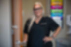 A medical assistant in black scrubs smiles while standing in the doorway of a patient room at an Ohio State outpatient care facility, ready to assist with patient care.