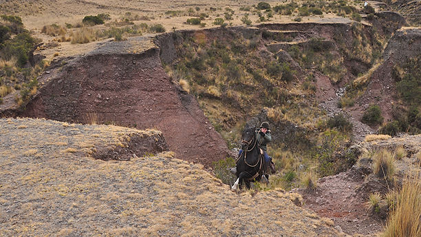 Woman riding on horseback through Andean mountain landscape in Peru.