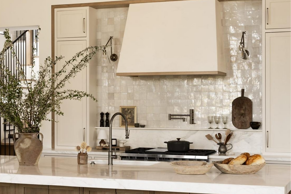 Cozy kitchen with rustic decor. Bread in wooden bowls on marble counter, black pot on stove, greenery in vase, bright tiled backsplash.