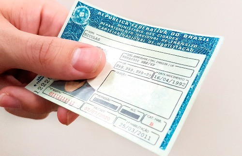 Imagem ilustrativa mostra uma Carteira Nacional de Habilitação segurada por uma mão de cor branca.