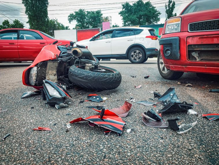 Imagem mostra uma moto vermelha caída na rua no meio de um acidente de trânsito envolvendo outros carros.