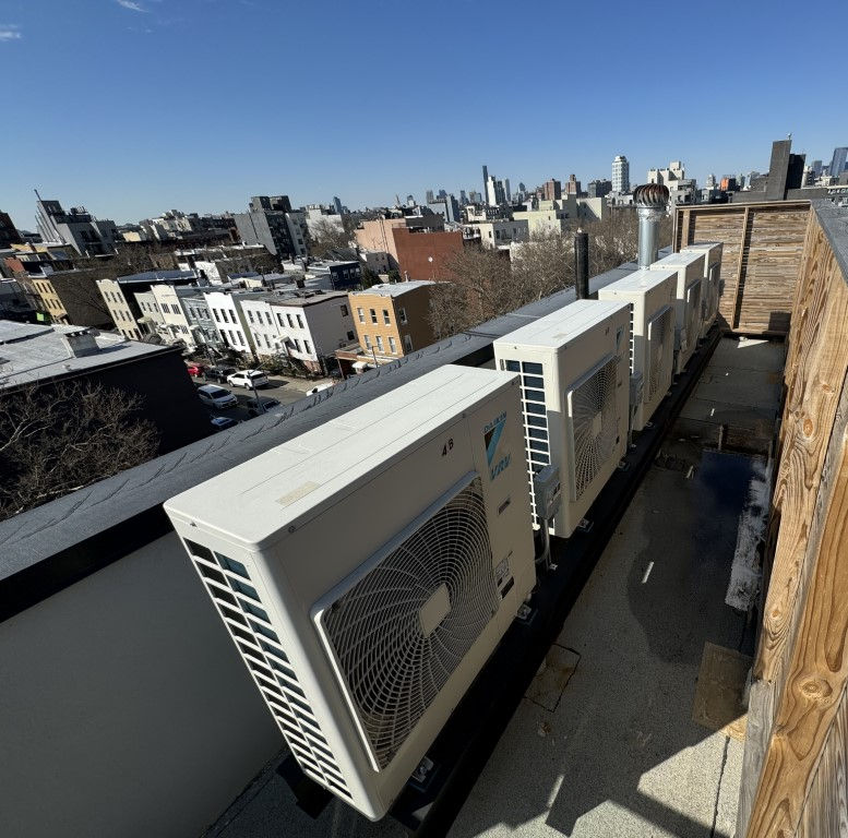 Rooftop with air conditioning units under a blue sky. Urban skyline in the background. Wood paneling on the right.