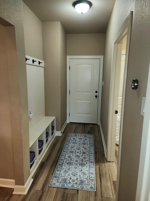 Hallway with a rug, white door and cabinets, and overhead lighting.