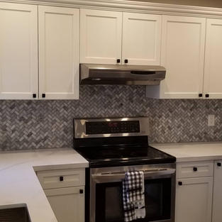 Installation of kitchen backsplash with grey herringbone tile grouted with grey grout. Kitchen with white cabinets, grey herringbone tile backsplash and white countertops.