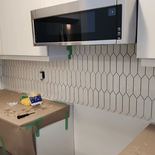 Installation of white picket tile backsplash in a kitchen with white cabinets.