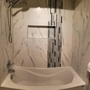Bathtub and tub surround makeover. New soaker tub tiled using 12"x24" white tiles with grey veins; installation of a shower niche, and finished with silver side trim. The new shower niche includes grey/black mosaic accent tiles.