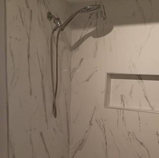 Tiling of bathroom tub surround using 12"x24" white tiles with grey veins, installing a shower niche, and finished with silver side trim.