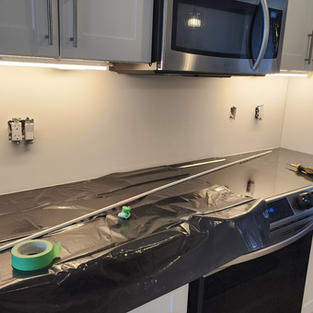 Kitchen with white cabinets; stainless steel range hood; backless, stainless steel stove; and black countertop.
