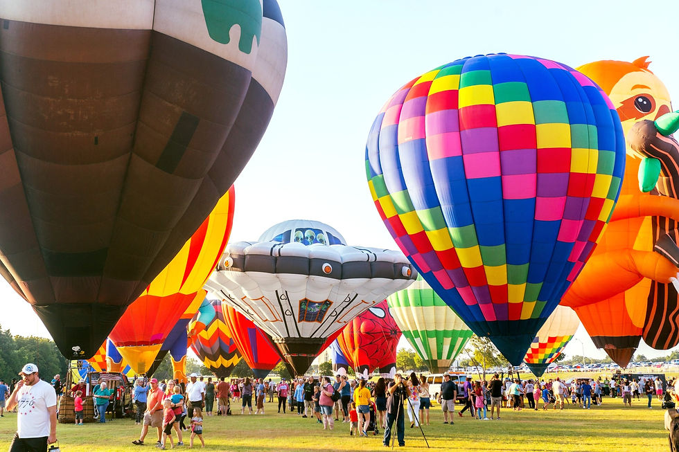 Crowd at a hot air balloon festival in Plano, Texas with giant colorful balloons inflating over a grassy field in bright daylight. Top things to do in Dallas during fall.