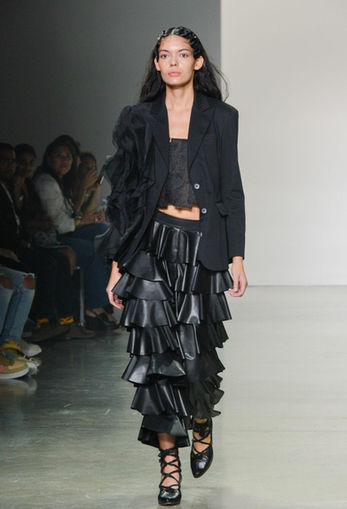 A female model modeling a all black look designed by SISIO walking down a runway